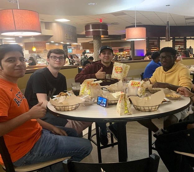 four men sitting around a table eating in the dining hall