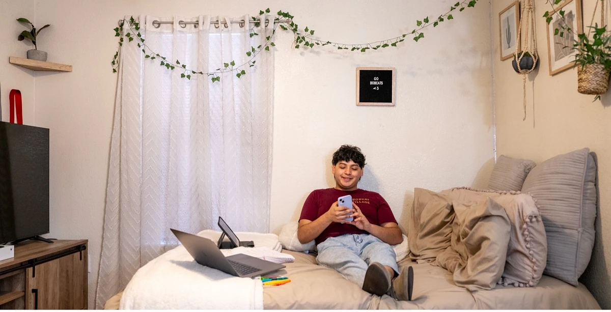 student sitting on their bed in residence hall room