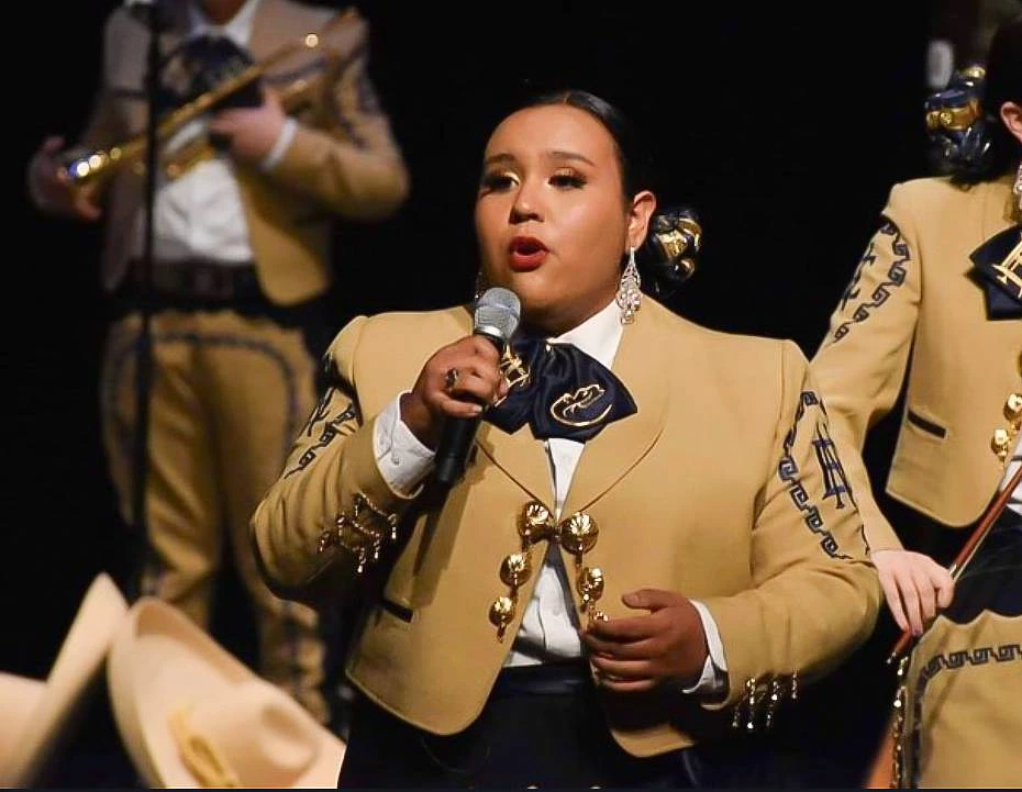 A performer in traditional mariachi attire is singing into a microphone.