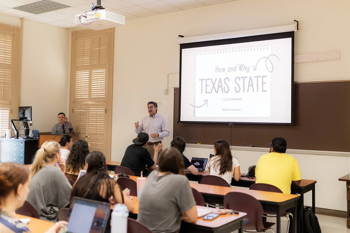 A man is giving a presentation titled "How and Why Texas State" to a classroom of attentive students.